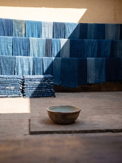 Bazaar Stall — Hard overhead sun cutting a stack of printed indigo.